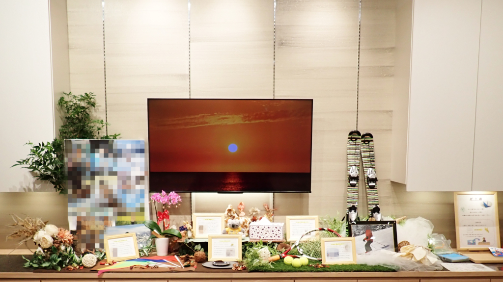 「スキー板やテニスラケットなどの愛用品や思い出の写真、夕日のモニター映像で故人らしさを演出した温かい家族葬・お別れ会のメモリアルスペース」
